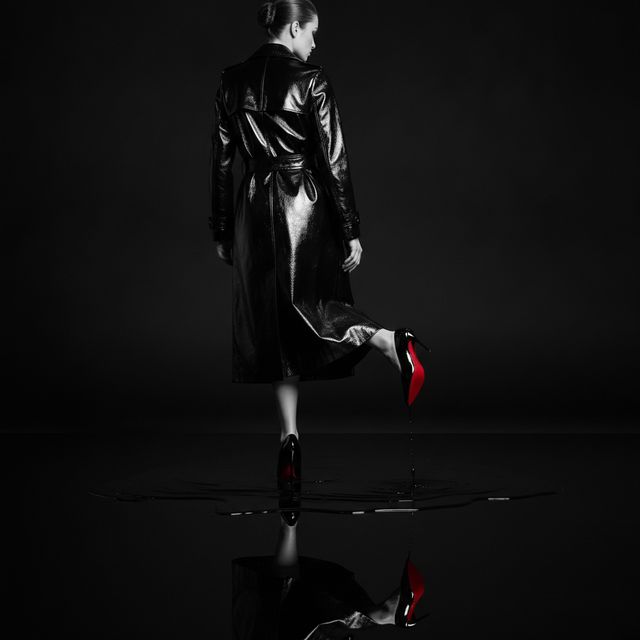 Redonnoir Fine-Art Foto ‚Fließender Lack‘ — elegante Frau in Schwarz mit rot lackierter Stiletto-Sohle, Liquid Lacquer, editorial Schwarzweiss mit rotem Farbakzent.